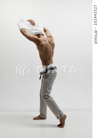 Portrait of muscular male fashion model taking off t-shirt isolated over white studio background. Man posing shirtless. Masculinity 101443527
