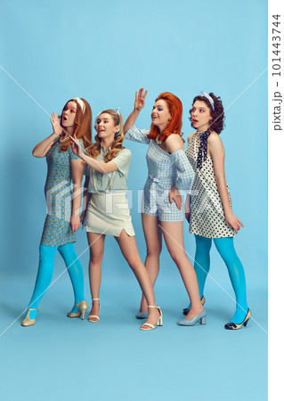 Greetings. Full-length portrait of beautiful young women posing in stylish clothes against blue studio background. Retro fashion, pin-up, 60s 101443744
