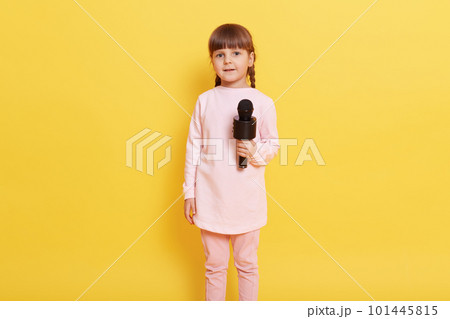 Littler attractive girl wearing pale pink casual clothing standing isolated over yellow background, full length photo of charming vocalist performing at concert, looks at camera with excited look. 101445815