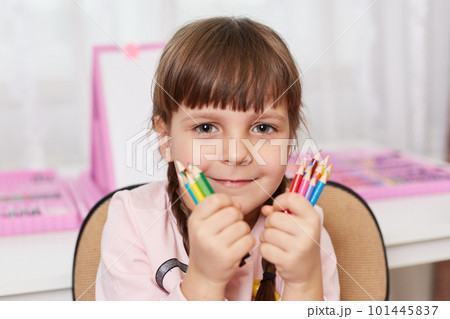Charming adorable female kid with two pigtails looking directly at camera, holds colored wax crayons in both hands, being happy, can painting, satisfied child being ready to draw. 101445837