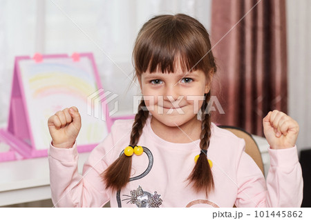 Cute little preschooler child drawing at home, small artist finished her picture, feels happiness, keeps fists clenched, looks at camera with satisfied facial expression. 101445862