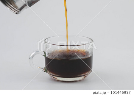 Pouring coffee from moka pot into transparent glass isolated on white background. Close-up of hand pouring freshly brewed drip coffee in a mug. Prepare alternative coffee. 101446957