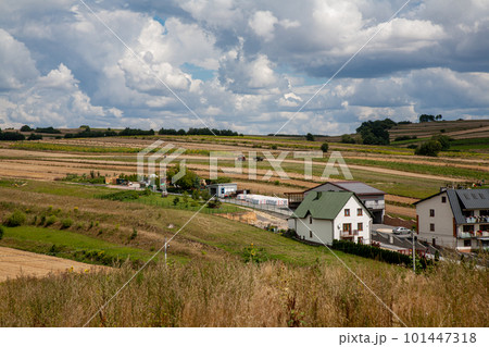 Farm village. Countryside scenery. Nature landscape. White cottage houses on meadow hills with yellow green field and fluffy sky clouds daylight panorama. Farm village. Countryside scenery. Nature landscape. White cottage houses on meadow hills with yellow green field and fluffy sky clouds daylight panorama. 101447318