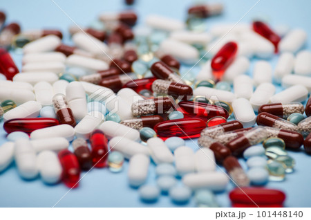 Background of multi-colored medical pills, tablets, dragees and translucent gel capsules, scattered on blue background. Close-up. Still life. Pharma business. Pharmaceutical industry. World Health Day Background of multi-colored medical pills, tablets, dragees and translucent gel capsules, scattered on blue background. Close-up. Still life. Pharma business. Pharmaceutical industry. World Health Day 101448140