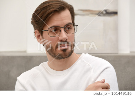 Close-up of a cheerful satisfied attractive man with stubble, with a wide smile, in round glasses, rejoices at success at work, stands against the backdrop of a cozy interior. Fashion designer happy 101449136