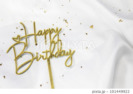 Happy Birthday text sign topper stick on white satin background, sparkling gold. Festive,celebration concept Happy Birthday text sign topper stick on white satin background, sparkling gold. Festive,celebration concept 101449922