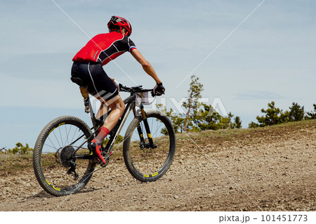 cross-country cycling, athlete cyclist riding mountain bike uphill on gravel road cross-country cycling, athlete cyclist riding mountain bike uphill on gravel road 101451773