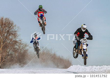 group motocross rider jumping on snowy springboard, winter off-road motorcycle racing 101451792