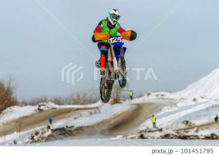 motocross rider jumping on snowy springboard, winter off-road motorcycle racing motocross rider jumping on snowy springboard, winter off-road motorcycle racing 101451795