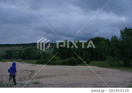A lonely boy runs across the dried-up ground to a green forest under storm clouds. Despair A lonely boy runs across the dried-up ground to a green forest under storm clouds. Despair 101453119