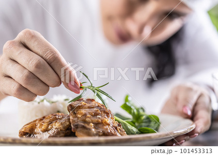 Close-up view of chef's fingers with rosemary sprig decorating food in restaurant kitchen 101453313