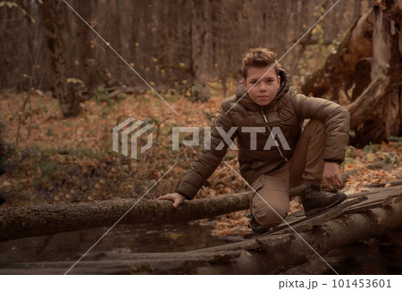 Boy sits on the wooden bridge over the river in fall forest. Brown toned. Boy sits on the wooden bridge over the river in fall forest. Brown toned. 101453601