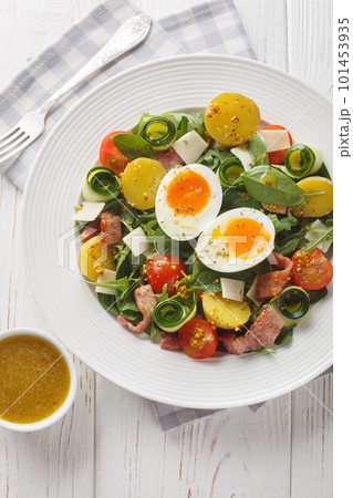 Peasant salad prepared with leafy vegetables, ham, cheese, tomatoes, potatoes and soft-boiled eggs closeup. Vertical top view Peasant salad prepared with leafy vegetables, ham, cheese, tomatoes, potatoes and soft-boiled eggs closeup. Vertical top view 101453935