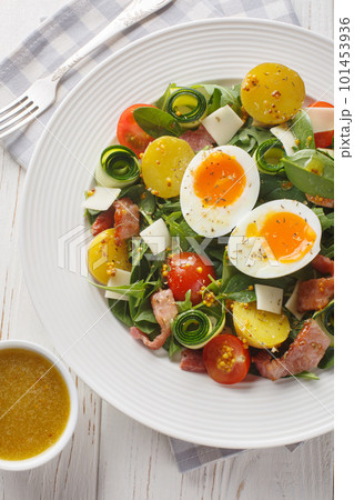 Summer fresh salad with potatoes, tomatoes, bacon, arugula, zucchini, cheese and soft-boiled eggs close-up on a plate. Vertical top view Summer fresh salad with potatoes, tomatoes, bacon, arugula, zucchini, cheese and soft-boiled eggs close-up on a plate. Vertical top view 101453936