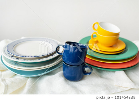 A pyramid of brightly colored bowls, plates and cups of different sizes and colors on the kitchen table. Scandinavian style, minimalism. Preparation for dinner with loved ones.t 101454339