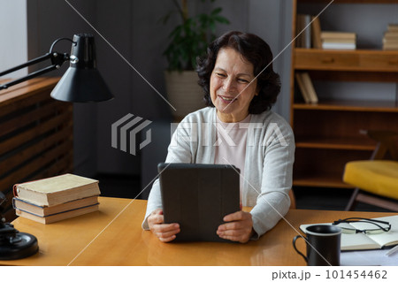 Happy middle aged senior woman holding tablet talk on video call with friends family. Laughing mature old senior grandmother having fun talking speaking with grown up children online Happy middle aged senior woman holding tablet talk on video call with friends family. Laughing mature old senior grandmother having fun talking speaking with grown up children online 101454462