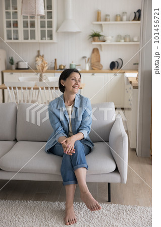 Cheerful attractive mature woman sitting on soft couch at home 101456721