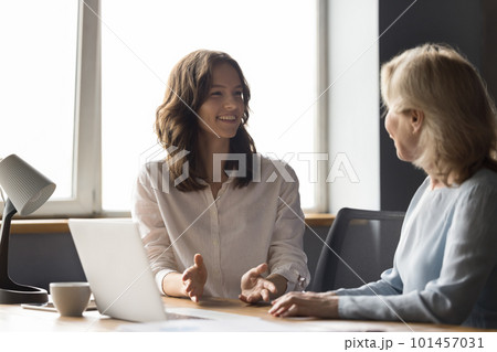 Two cheerful different aged business colleagues chatting at work table Two cheerful different aged business colleagues chatting at work table 101457031