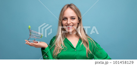 horizontal photo of stylish european woman shopper in green shirt with supermarket trolley on blue horizontal photo of stylish european woman shopper in green shirt with supermarket trolley on blue 101458129
