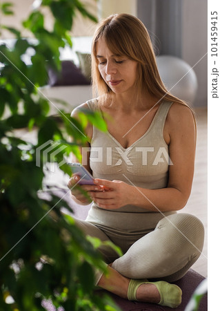 Trainer relaxing on yoga mat with smartphone after her workout in her pilates studio, checking new videos online. Caucasian woman taking break after yoga practice. Active lifestyle concept. Trainer relaxing on yoga mat with smartphone after her workout in her pilates studio, checking new videos online. Caucasian woman taking break after yoga practice. Active lifestyle concept. 101459415
