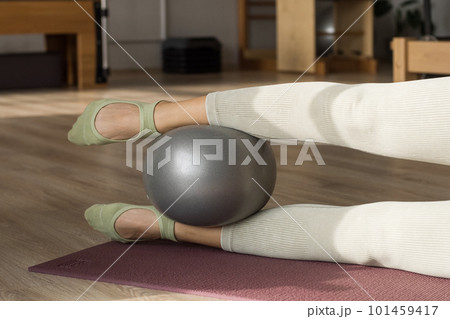 Pilates drill with mini-ball. Woman in sportswear using a small fit ball in pilaes yoga studio. Trainer holding fitness ball between legs Pilates drill with mini-ball. Woman in sportswear using a small fit ball in pilaes yoga studio. Trainer holding fitness ball between legs 101459417