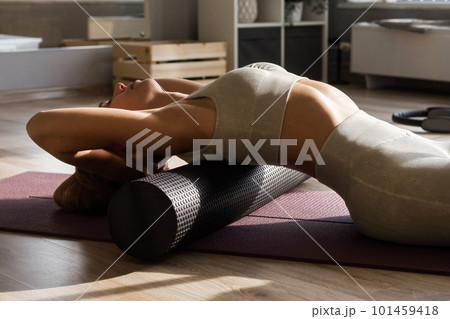 Fitness concept. Close up of woman relaxing after workout on the exercising yoga mat. Portrait of Active Woman Using Foam Roller for back and spine exercise 101459418
