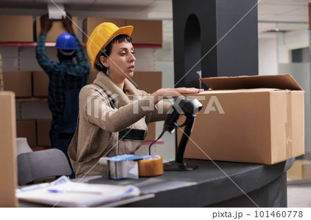 Retail storehouse manager packing cardboard box at counter desk and closing package. Caucasian warehouse worker wearing safety helmet preparing customer parcel for delivery Retail storehouse manager packing cardboard box at counter desk and closing package. Caucasian warehouse worker wearing safety helmet preparing customer parcel for delivery 101460778