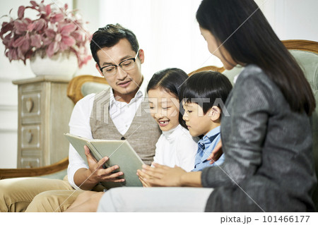 young asian parents and two children sitting on couch reading book together in family living room at home young asian parents and two children sitting on couch reading book together in family living room at home 101466177