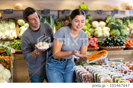 Man and woman choosing packaged carrots and sliced papaya to buy in fruit and vegetables shop 101467847