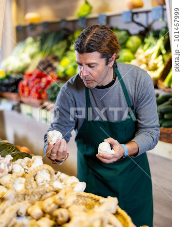 Male seller holding garlic standing in fruit and vegetable section of supermarket 101467999