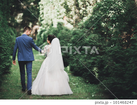 Stylish couple of happy newlyweds walking in the park on their wedding day with bouquet 101468247