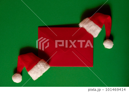 Santa hat with empty paper card note envelope on green background. Copy space for your text. Mock up for advertisement. Holiday Christmas composition 101469414