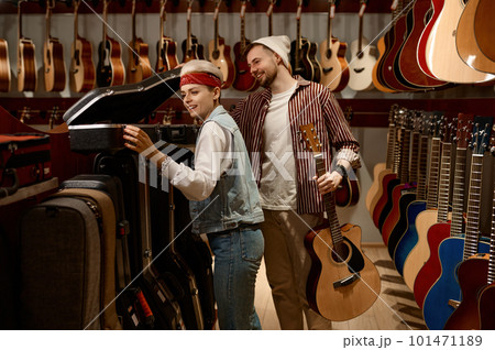 Seller woman helping man buyer to choose guitar case at music store 101471189