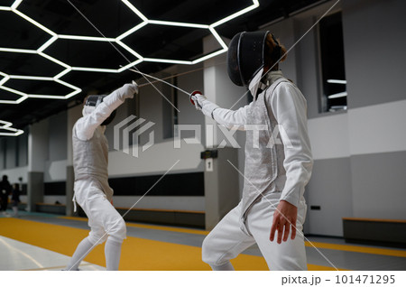 Athletes in uniforms and protective helmet mask fighting duel with rapiers 101471295