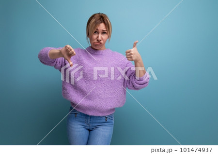 distressed upset blond young woman in purple hoodie showing like and dislike on blue background with 101474937