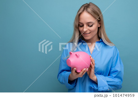 attractive blond girl holding a piggy bank on a blue isolated background attractive blond girl holding a piggy bank on a blue isolated background 101474959