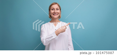 stylish blond middle-aged woman in a white blouse demonstrates something on a studio background with stylish blond middle-aged woman in a white blouse demonstrates something on a studio background with 101475087