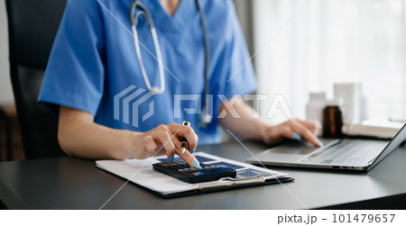 Healthcare costs and fees concept.Hand of smart doctor used a calculator and smartphone, tablet for medical costs at hospital in morning light 101479657