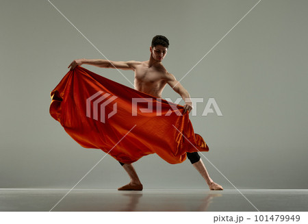 Dynamic image of handsome, artistic, young man, ballet dancer performing with red silk fabric against grey studio background Dynamic image of handsome, artistic, young man, ballet dancer performing with red silk fabric against grey studio background 101479949