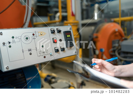 A female worker with a folder and a pen in her hand, writing meter readings. In the background-boiler room. Industrial production. Close up A female worker with a folder and a pen in her hand, writing meter readings. In the background-boiler room. Industrial production. Close up 101482283