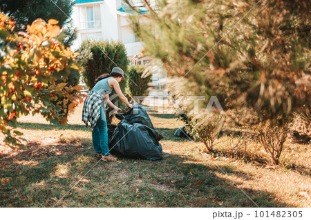The concept of environmental pollution and Earth day. Woman volunteer doing cleaning in the Park in front of the house. She's putting the garbage bags in one pile. Copy space 101482305