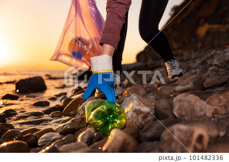 Volunteer collects plastic bottles on the ocean's beach. Cleaning of the coastal zone and preservation of ecology. Concept of conservation of ecology and garbage collection for recycling 101482336