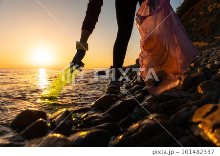 Earth day. A volunteer take a plastic bottle by the sea or river holding a plastic trash bag. Concept of coastal cleanup 101482337