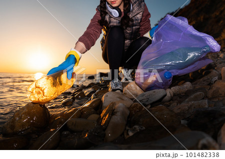 A female volunteer picks up garbage on the ocean. Cleaning of the coastal zone and preservation of ecology. Trash collection for recycling. Concept of Earth Day 101482338