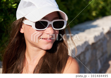 Teen girl with freckles in a white cap with sunglasses on the beach. 101484495