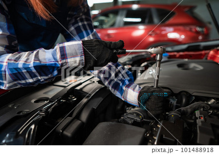 Female auto mechanic unscrewing a nut to replace a car spark plug. 101488918