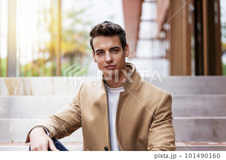 Portrait of stylish handsome young man with coat sitting outdoors 101490160