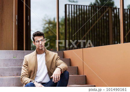 Portrait of stylish handsome young man with coat sitting outdoors 101490161