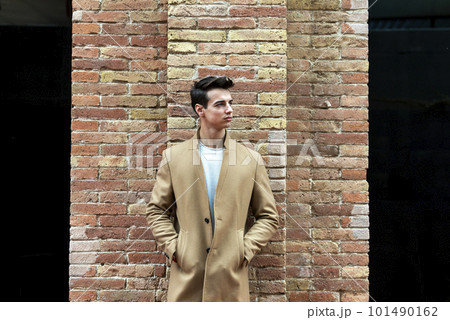Young man wearing winter clothes in the street. Young guy with modern hairstyle with brown coat. 101490162