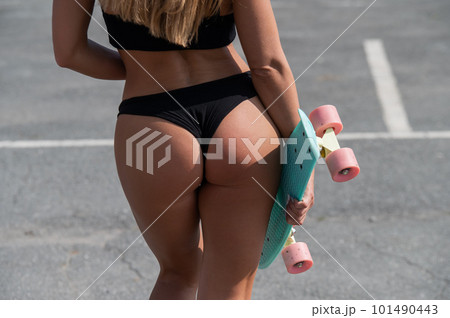 Close-up of the buttocks of a caucasian woman in a swimsuit holding a penny board. Athletic girl with a seductive figure.  Close-up of the buttocks of a caucasian woman in a swimsuit holding a penny board. Athletic girl with a seductive figure.  101490443